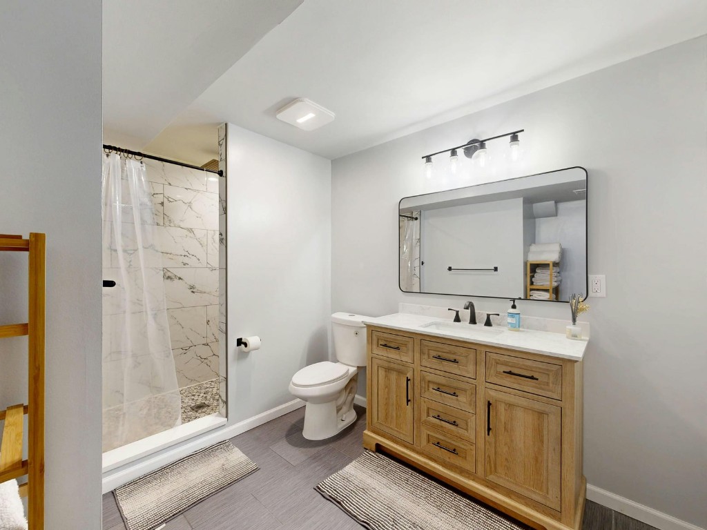 Modern bathroom with light wood vanity, marble countertop, and walk-in shower with marble tile