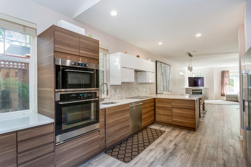 Modern open-concept kitchen with wood-grain cabinets, white uppers, marble backsplash, and stainless appliances