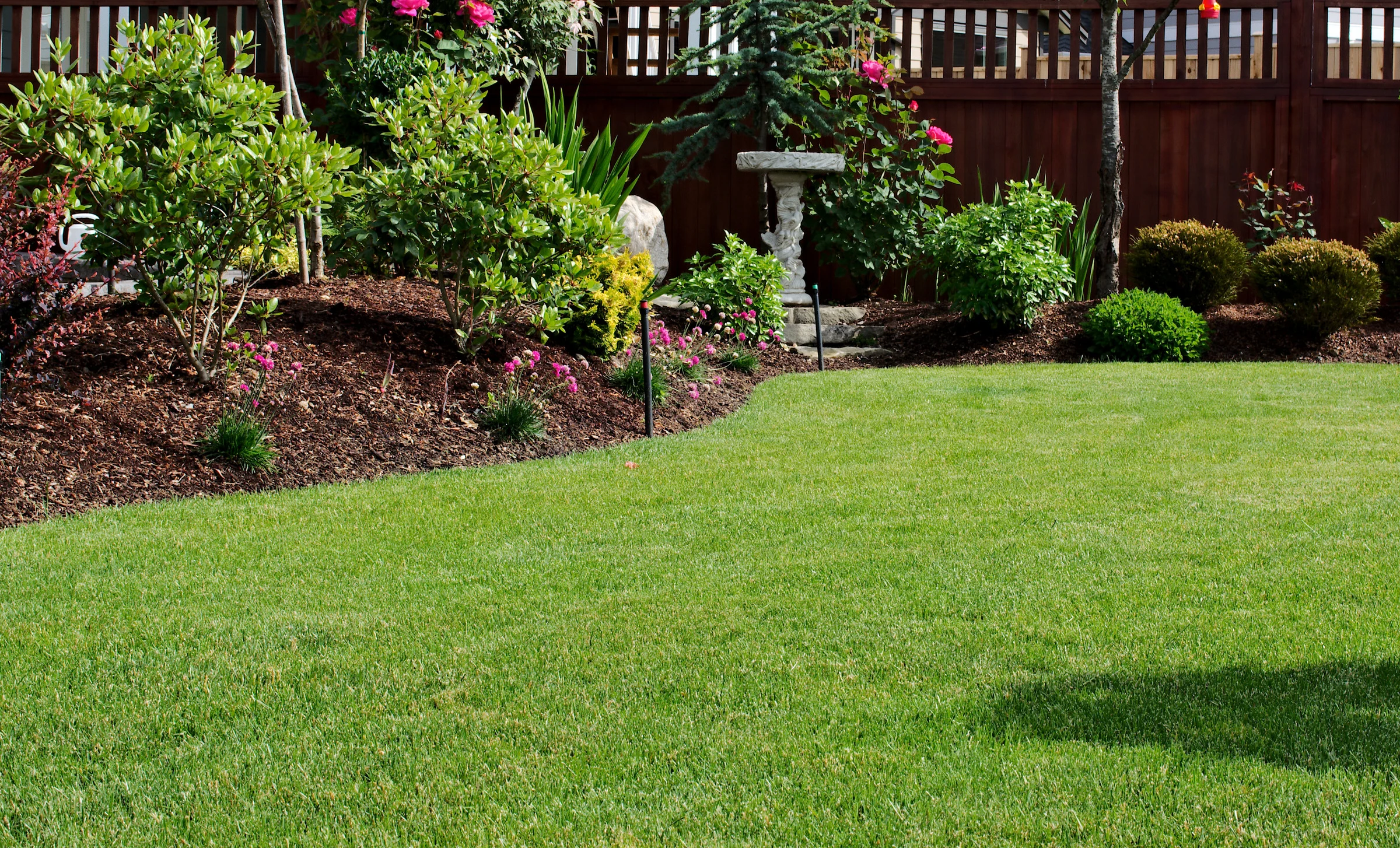 Residential backyard with mulched garden beds and a healthy green lawn