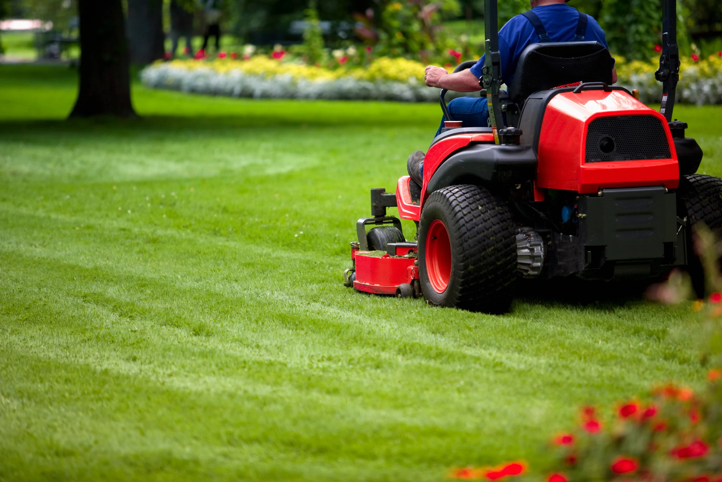 Operator mowing a large lawn with a zero-turn mower leaving striped patterns
