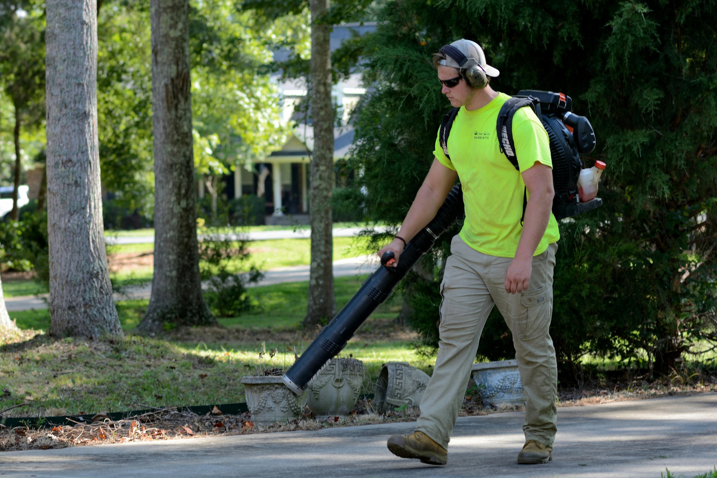 Worker in safety gear using a backpack leaf blower along a driveway